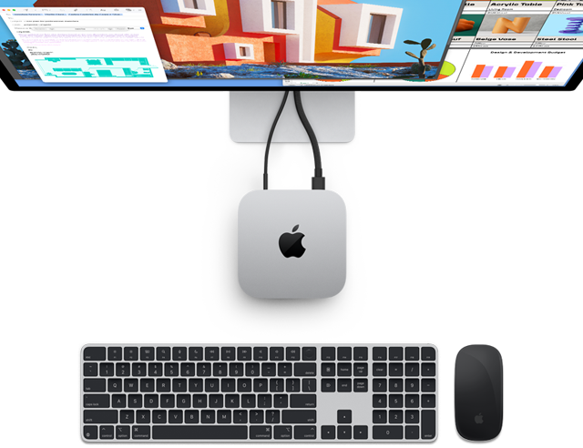 Top of silver Mac mini with Apple logo,shown plugged into a monitor and next to a wireless Magic Keyboard and Magic Mouse
